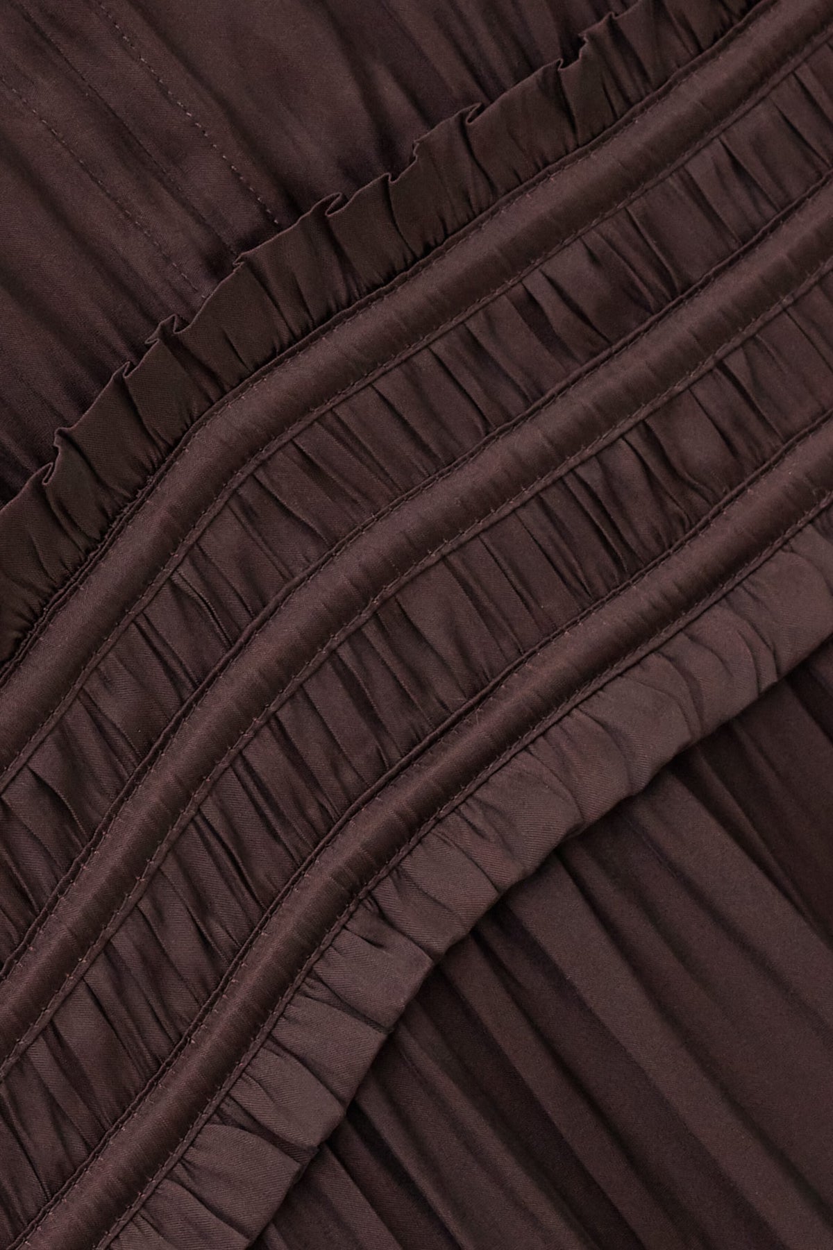 Close-up of a dark brown pleated fabric with horizontal ruffled trim and gathered seams.