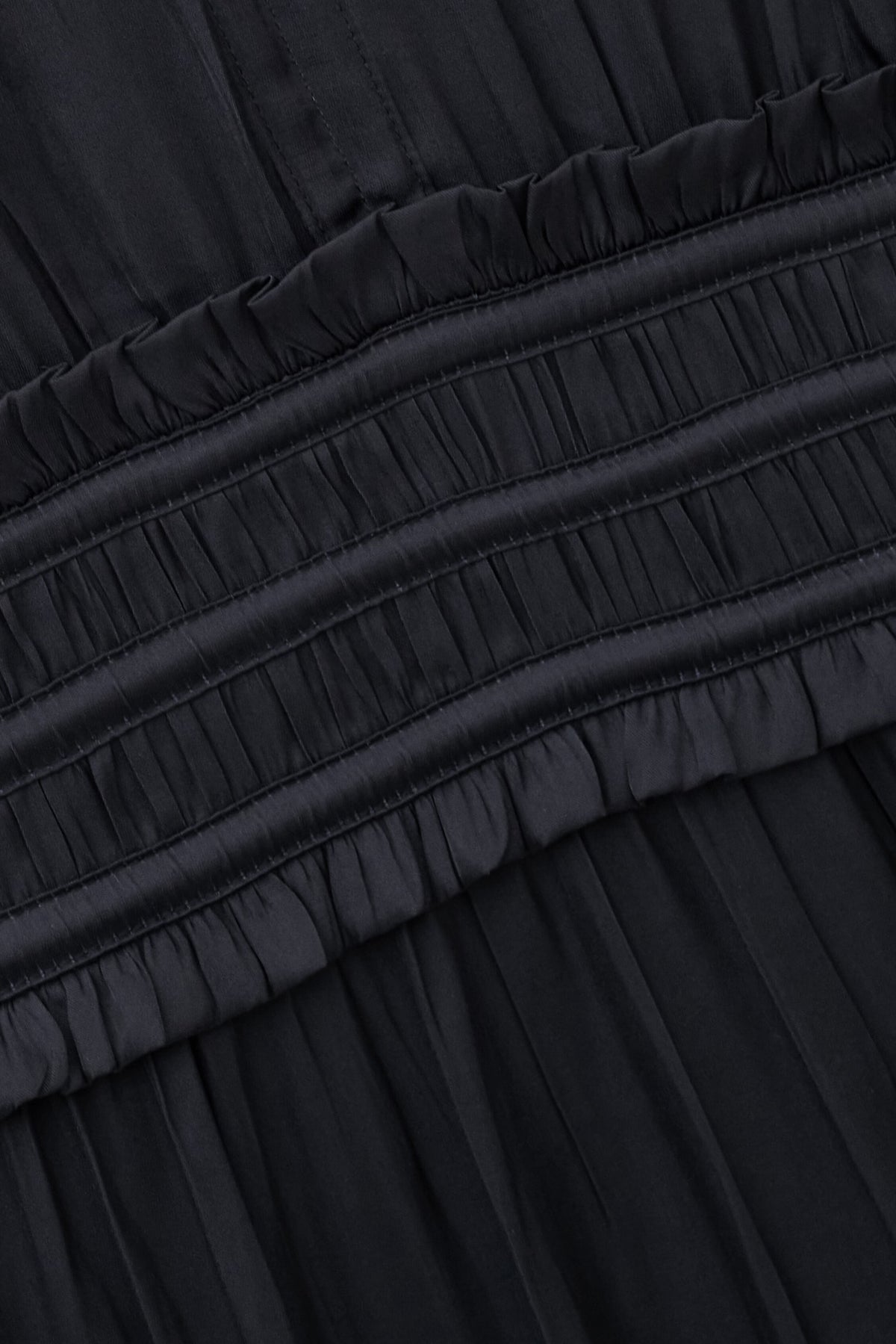 Close-up of a black pleated fabric garment with a gathered elastic waistband and ruffled trim.