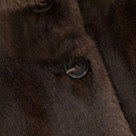 Close-up of a dark brown fur or faux-fur garment with a button closure and soft textured surface.