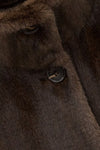 Close-up of a dark brown fur or faux-fur garment with a button closure and soft textured surface.