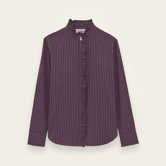 A long-sleeve button-up shirt in a deep purple color with thin white vertical pinstripes, featuring a high stand collar and a decorative ruffled trim down the front placket, shown against a light off-white background.