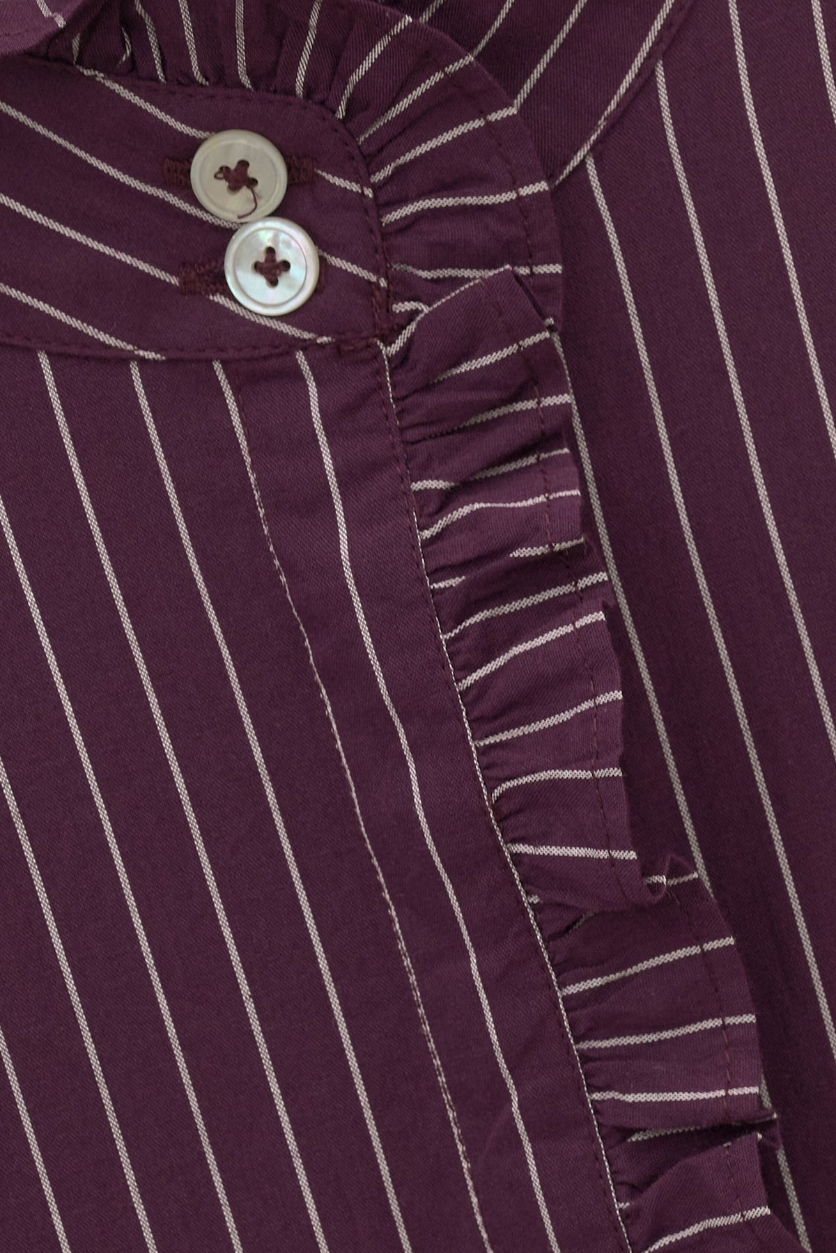 Close-up of a dark purple and white vertically striped ruffled blouse with decorative buttons.