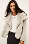 A model wearing a light gray fuzzy faux fur jacket over a white t-shirt and dark pinstripe trousers, photographed against a plain off-white background.