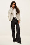 A model wearing a light gray fuzzy faux fur jacket over a white t-shirt and dark pinstripe trousers, photographed against a plain off-white background.