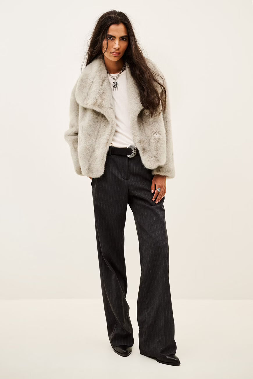 A model wearing a light gray fuzzy faux fur jacket over a white t-shirt and dark pinstripe trousers, photographed against a plain off-white background.