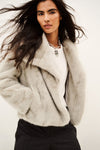 A model wearing a light gray fuzzy faux fur jacket over a white t-shirt and dark pinstripe trousers, photographed against a plain off-white background.