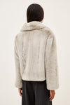 A model wearing a light gray fuzzy faux fur jacket over a white t-shirt and dark pinstripe trousers, photographed against a plain off-white background.