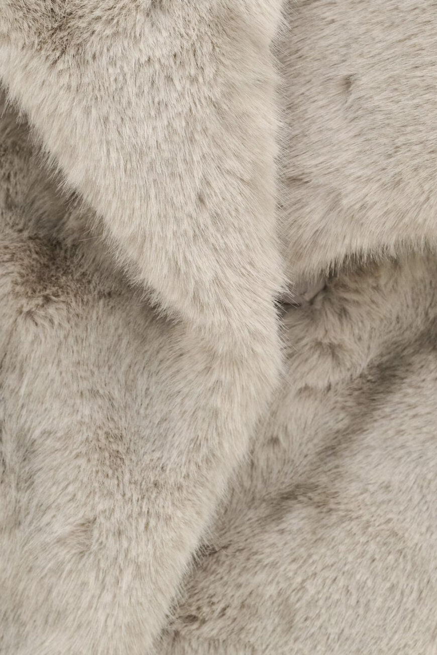A close-up of plush faux fur fabric in a light warm gray or greige tone, showing the soft texture and layered folds of the material.