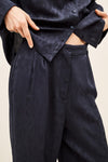 Close-up of a person wearing dark navy wide-leg trousers and a matching dark navy button-up shirt, with hands adjusting the shirt and pulling the fabric to show texture.