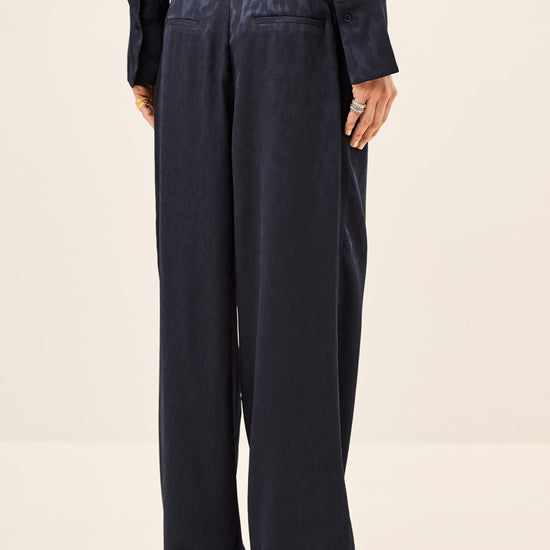 A person shown from the back wearing dark navy wide-leg trousers and a matching dark top against a plain light beige studio background.