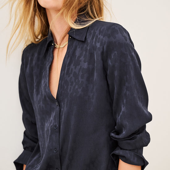 Woman wearing blue shirt and black trousers on white background side view