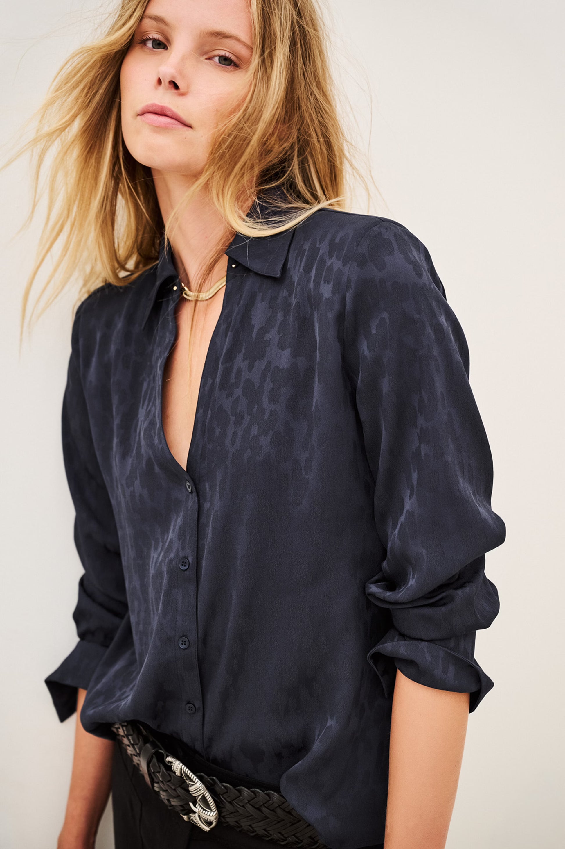 Woman wearing blue shirt and black trousers on white background side view