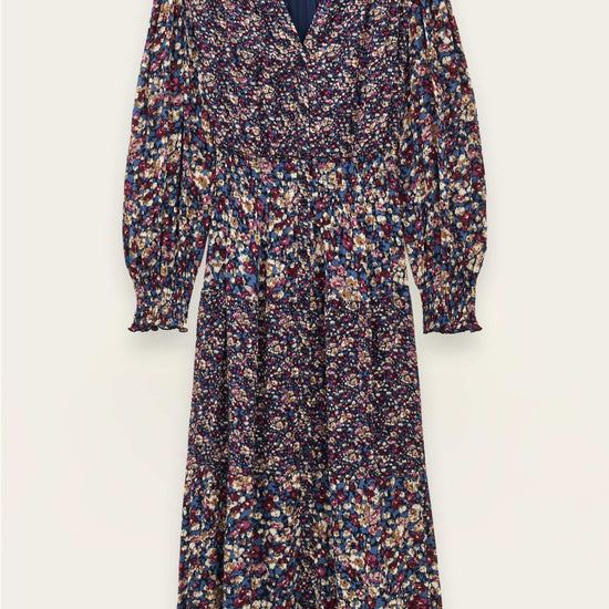 A long-sleeve midi dress with a dense multicolor floral print on a dark navy base, featuring a V-neckline and gathered waist, shown flat against a light cream background.