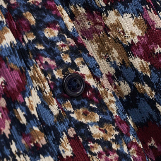 Close-up of a textured fabric with an abstract ikat pattern in navy blue, burgundy, beige, and brown, featuring a dark button.