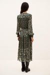 A woman viewed from the back wearing a long-sleeve midi dress with a dense dark green and beige floral print, paired with black ankle boots, against a plain white studio background.
