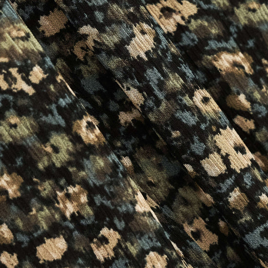 Close-up of a textured fabric with a dense abstract floral or pixelated pattern in black, olive green, beige, and muted blue-gray.
