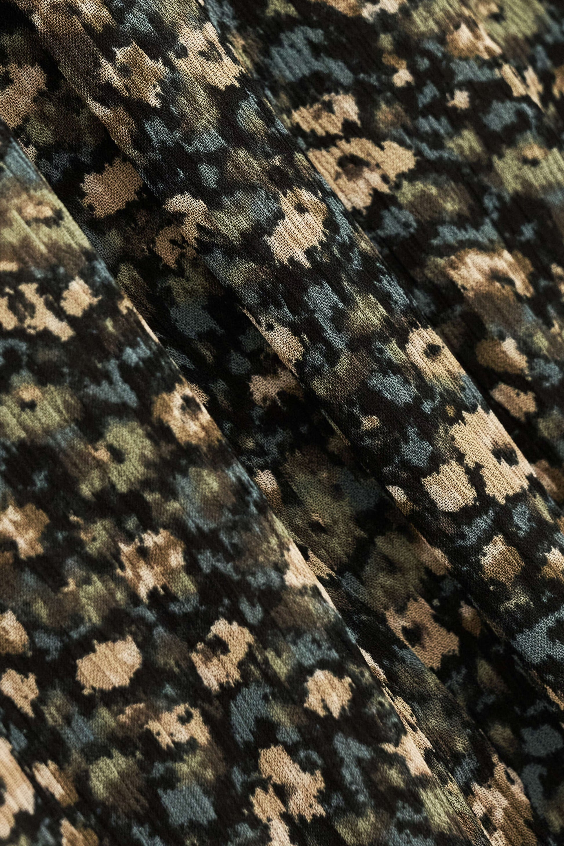 Close-up of a textured fabric with a dense abstract floral or pixelated pattern in black, olive green, beige, and muted blue-gray.