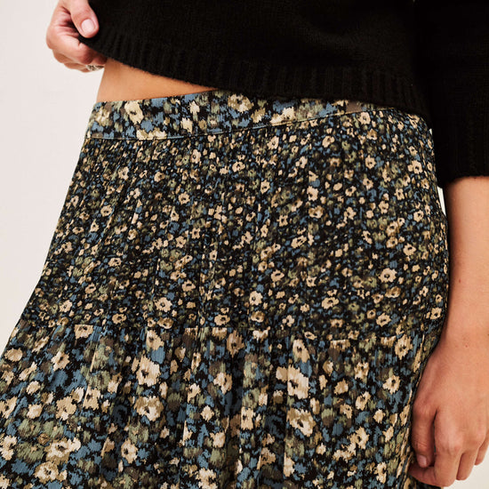 Close-up of a person wearing a black knit sweater and a dark floral skirt with blue, beige, and cream flowers, against a plain light background.