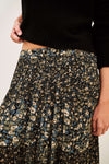Close-up of a person wearing a black knit sweater and a dark floral skirt with blue, beige, and cream flowers, against a plain light background.