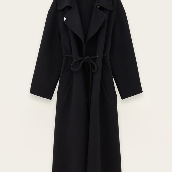 A long dark blue wool-blend coat with a tie belt, wide lapels, and front patch pockets, shown flat against a light off-white background.