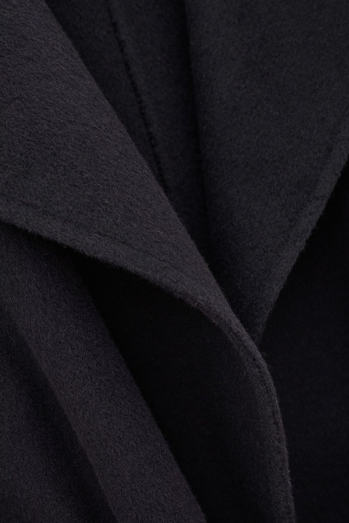 Close-up of a dark charcoal gray or black textured fabric with soft draped folds and a fine woven surface.