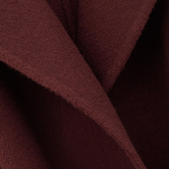 A close-up of draped burgundy wool fabric with soft folds and a fine napped texture.