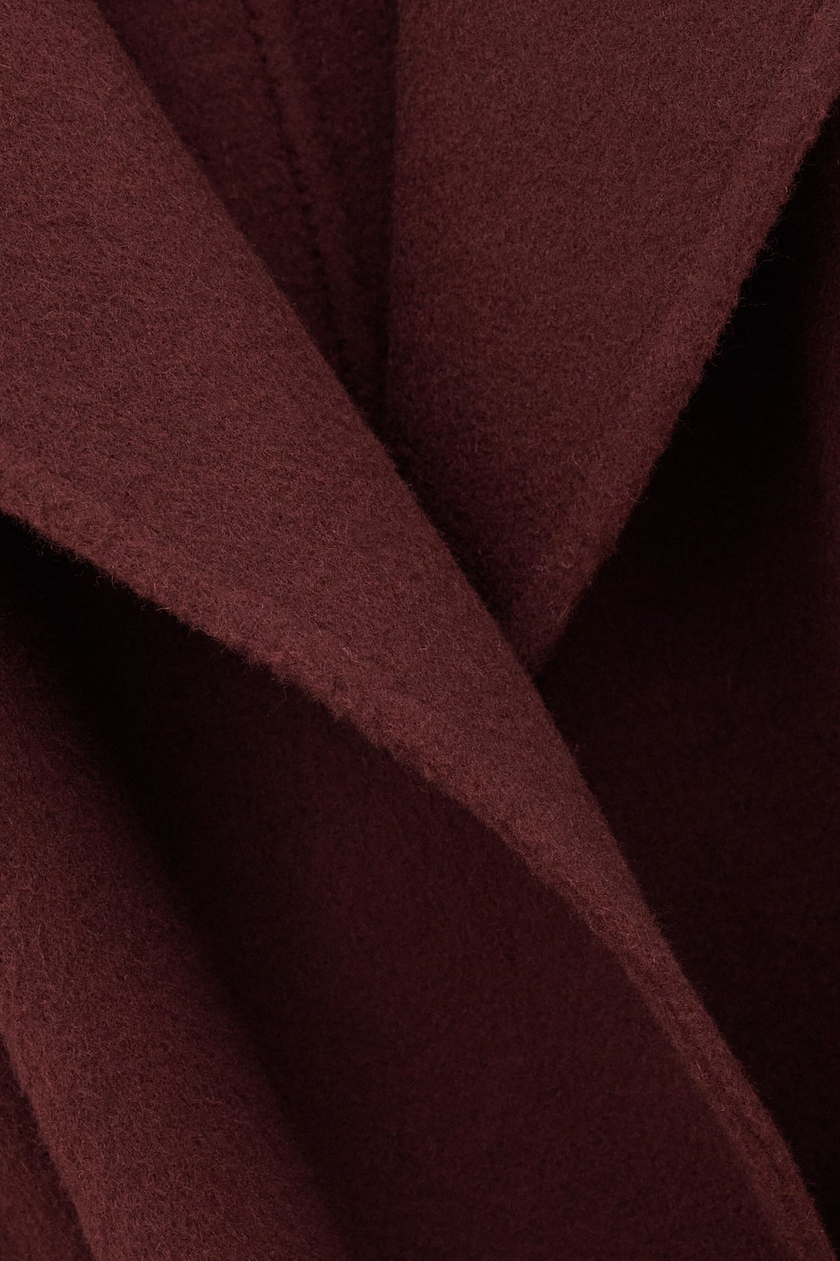 A close-up of draped burgundy wool fabric with soft folds and a fine napped texture.