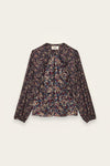 A long-sleeve blouse with a dense multicolor floral and abstract print on a dark base, featuring a gathered front and a round neckline, shown flat against a light cream background.