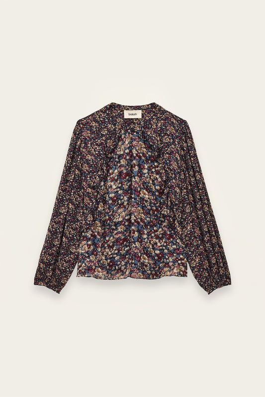 A long-sleeve blouse with a dense multicolor floral and abstract print on a dark base, featuring a gathered front and a round neckline, shown flat against a light cream background.
