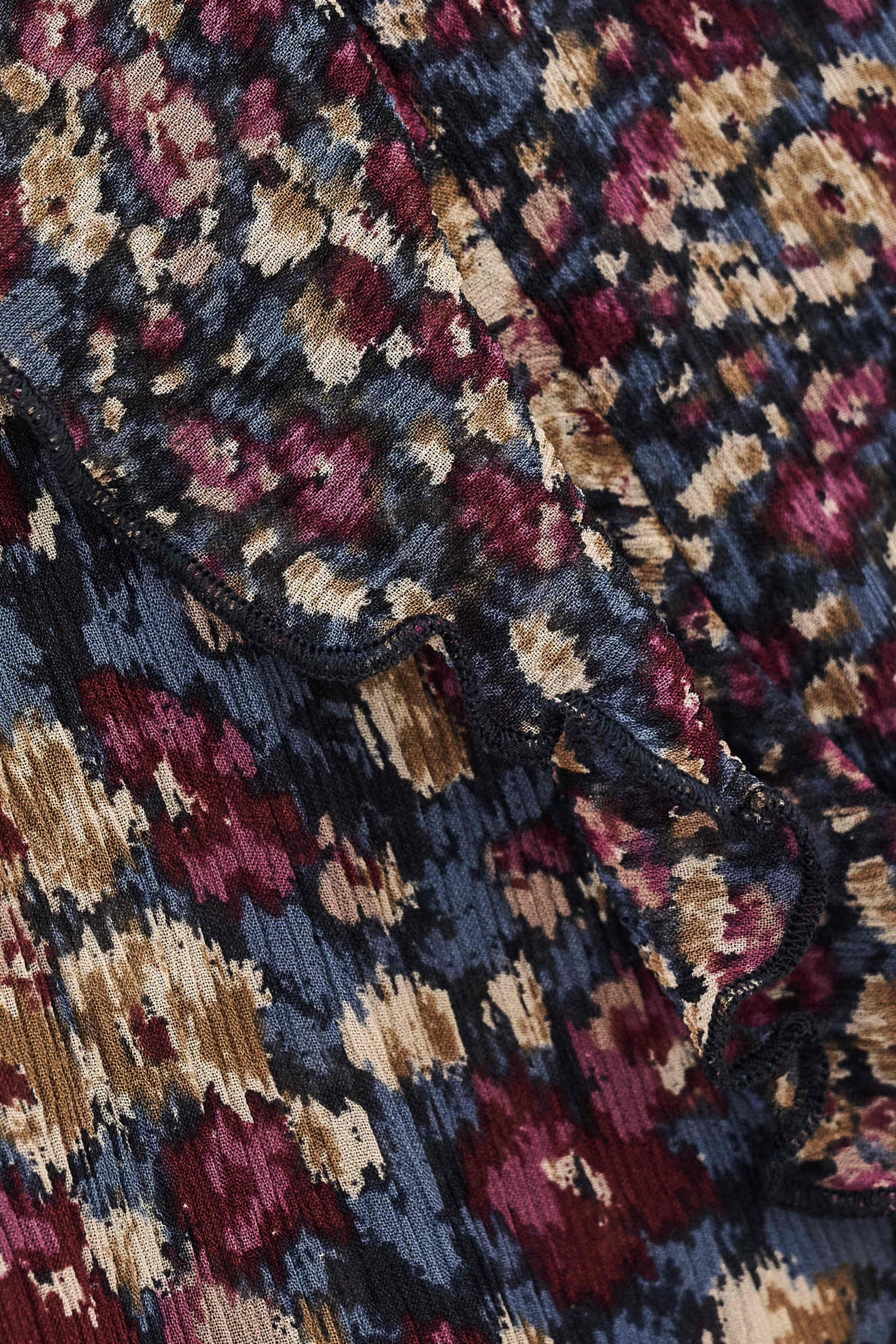 Close-up of a textured jacquard fabric with an abstract floral pattern in navy blue, burgundy, beige, and muted gold.
