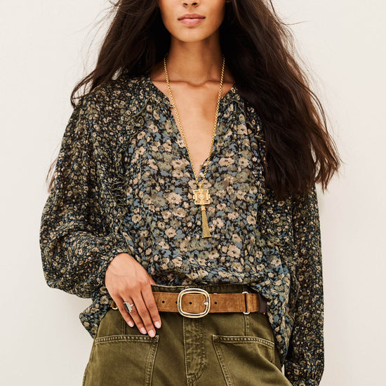 A woman modeling a long-sleeve floral blouse with a deep V-neck and a gold cross pendant, paired with olive green cargo pants and a brown belt, against a plain off-white background.
