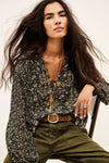 Woman sitting on a chair wearing a floral blouse and green trousers