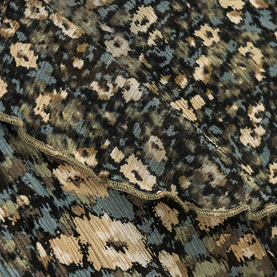 Close-up of a patterned textile with an abstract floral or ikat-style print in black, beige, muted blue-gray, and olive tones, with a scalloped edge visible across the middle.