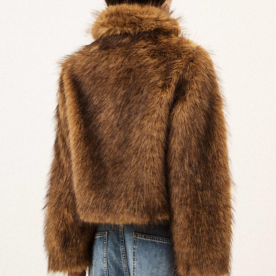 A model viewed from behind wearing a cropped brown faux fur jacket with a wide collar and blue jeans, set against a plain off-white background.