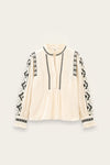 An off-white long-sleeve blouse with black geometric embroidered patterns along the neckline, front placket, and sleeves, displayed flat against a light beige background.