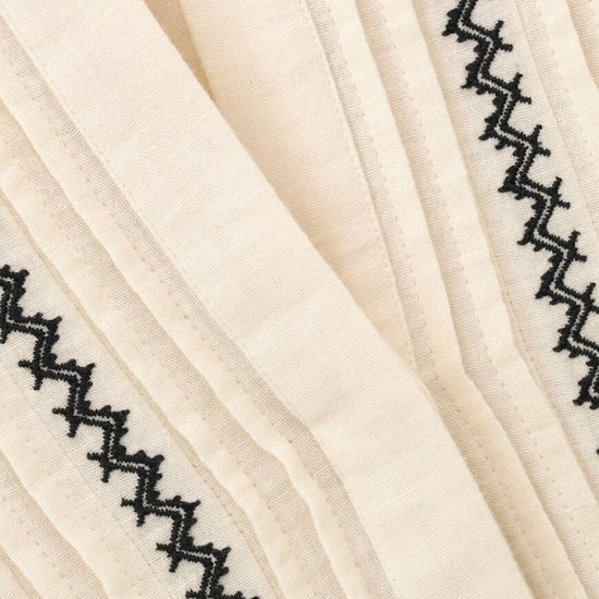 Close-up of a cream-colored pleated fabric with black zigzag embroidered borders.