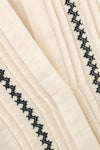 Close-up of a cream-colored pleated fabric with black zigzag embroidered borders.