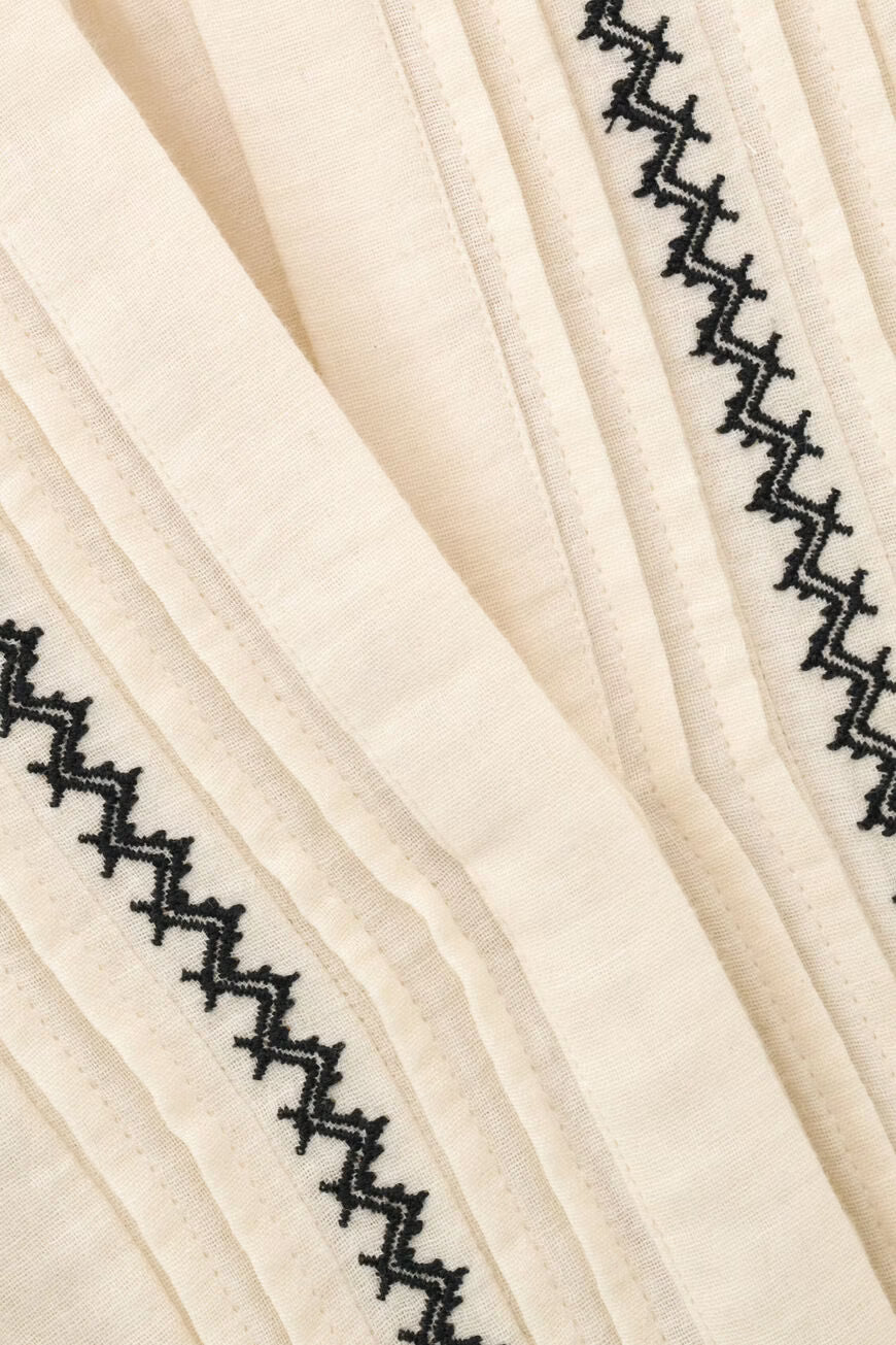 Close-up of a cream-colored pleated fabric with black zigzag embroidered borders.