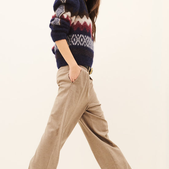 Woman wearing beige tailored trousers and a sweatshirt on a white background side view