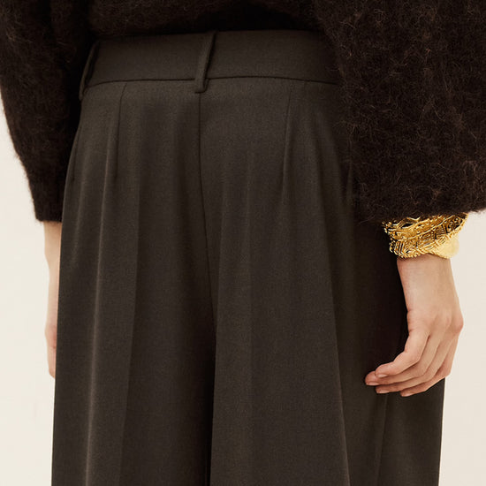 Woman wearing brown trousers and jumper on a white background close up rear view