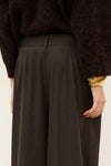 Woman wearing brown trousers and jumper on a white background close up rear view