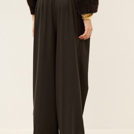 Woman wearing brown trousers and jumper on a white background rear view