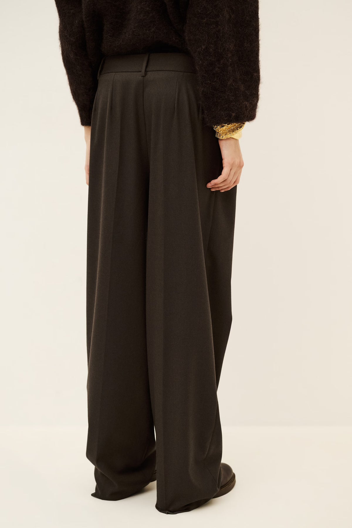 Woman wearing brown trousers and jumper on a white background rear view