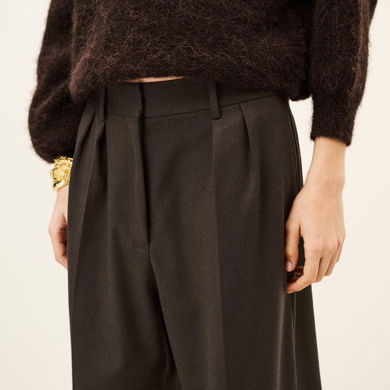 Woman wearing brown trousers and jumper on a white background close up of front