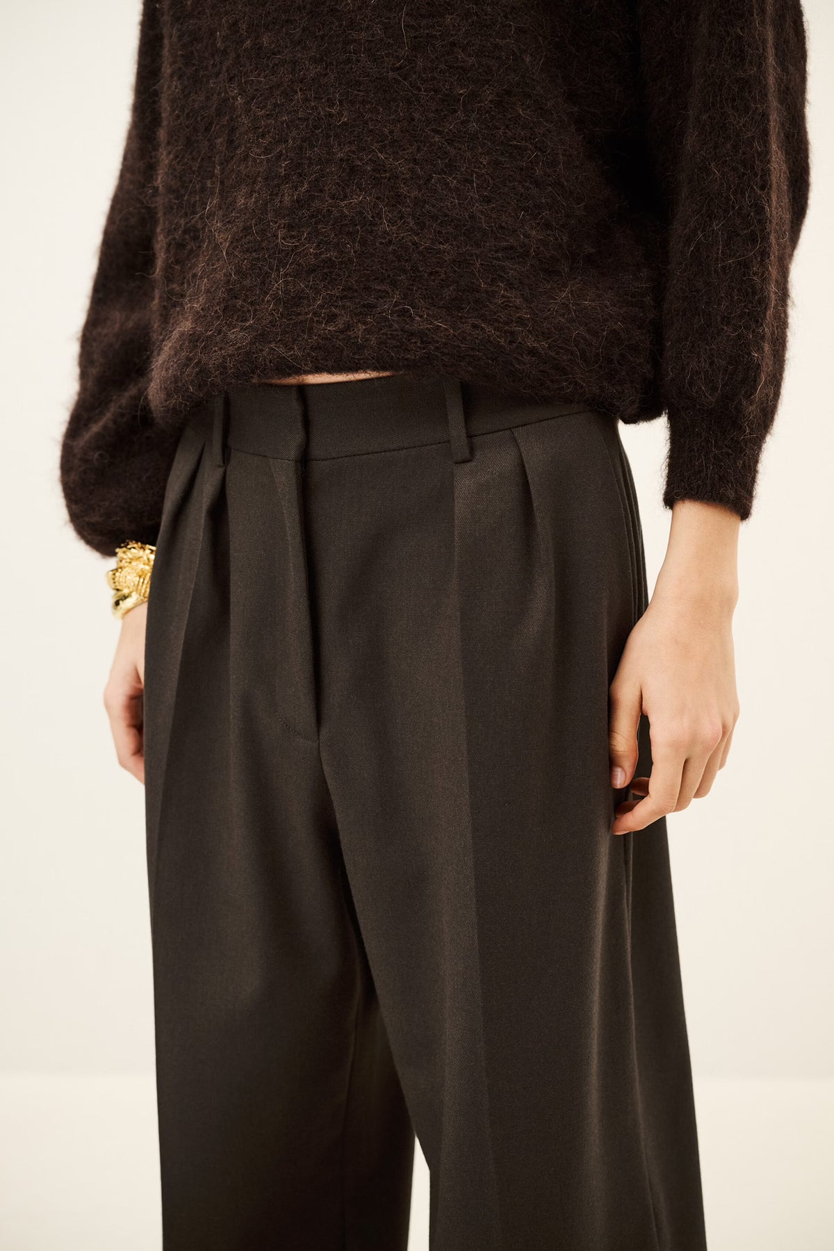 Woman wearing brown trousers and jumper on a white background close up of front