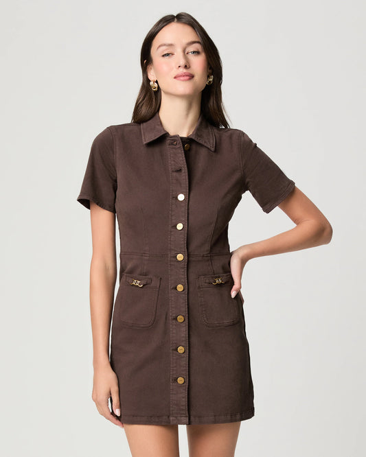 A woman modeling a short-sleeve brown shirt dress with gold-tone buttons and flap pockets, photographed against a light gray studio background.