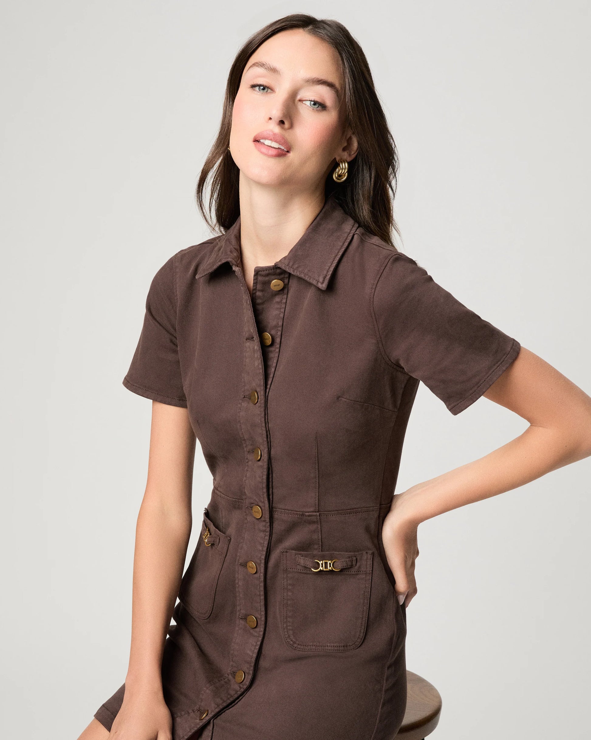 Woman wearing a brown short-sleeve shirt with buttons on a light gray background