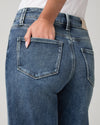 Close-up back view of a person wearing medium-wash blue denim jeans, with one hand tucked into the back pocket.