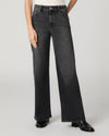 A model wearing a pair of wide-leg dark gray denim jeans with a faded wash, paired with black leather boots against a light gray studio background.