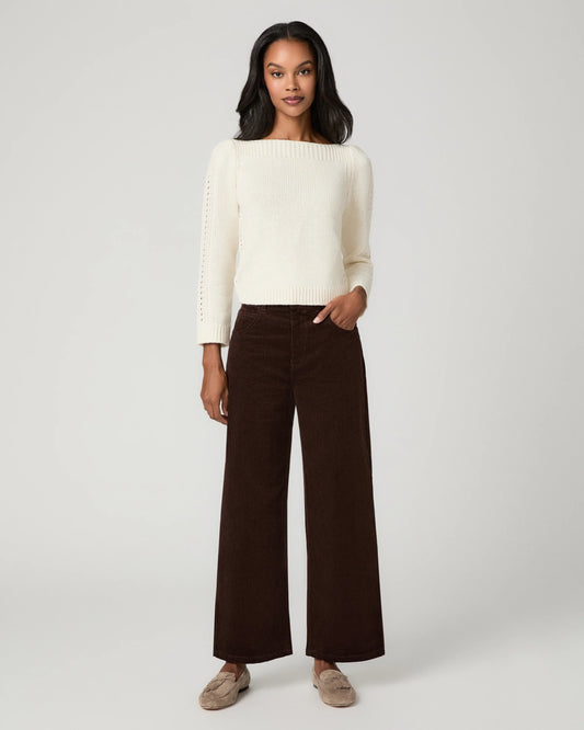 A woman modeling a cream knit sweater with textured sleeve details and dark brown wide-leg corduroy pants, paired with beige slip-on shoes, against a light gray studio background.